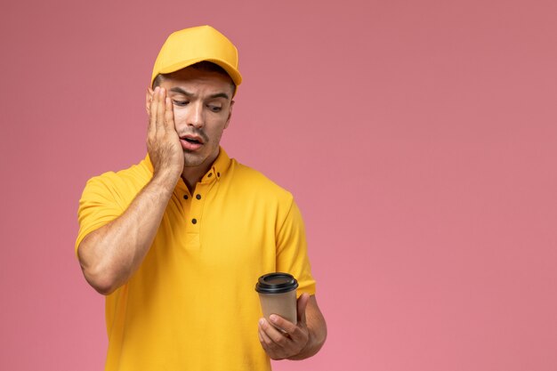 분홍색 책상에 갈색 커피 배달 컵을 들고 노란색 제복을 입은 전면보기 남성 택배