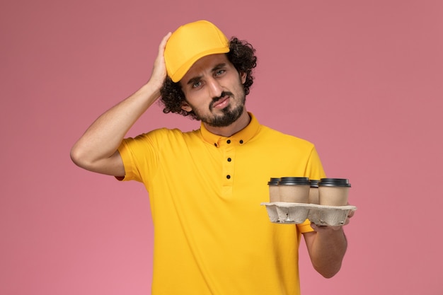 분홍색 벽에 생각 갈색 배달 커피 컵을 들고 노란색 제복을 입은 전면보기 남성 택배