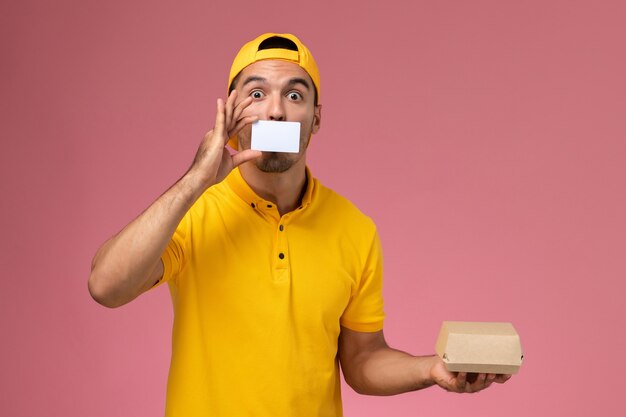 분홍색 배경에 카드와 작은 음식 패키지를 들고 노란색 유니폼에 전면보기 남성 택배.