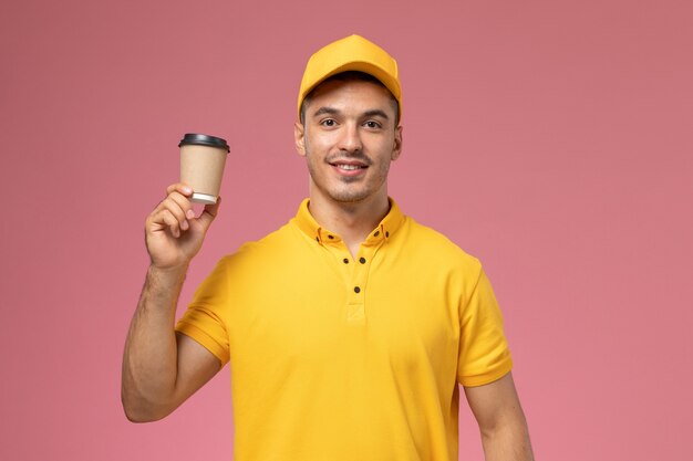Вид спереди мужской курьер в желтой форме с чашкой доставки кофе на розовом фоне