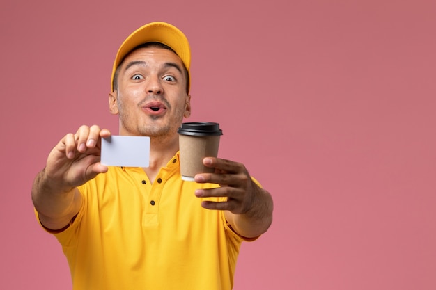ピンクの背景に配信のコーヒーカップと白いカードを保持している黄色の制服を着た正面男性宅配便