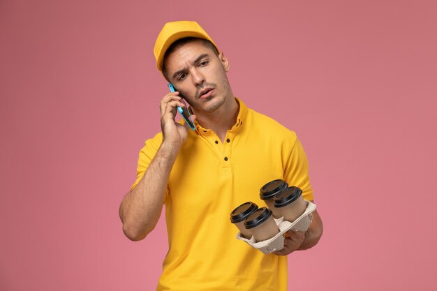 분홍색 책상에 전화로 얘기 배달 커피 컵을 들고 노란색 제복을 입은 전면보기 남성 택배