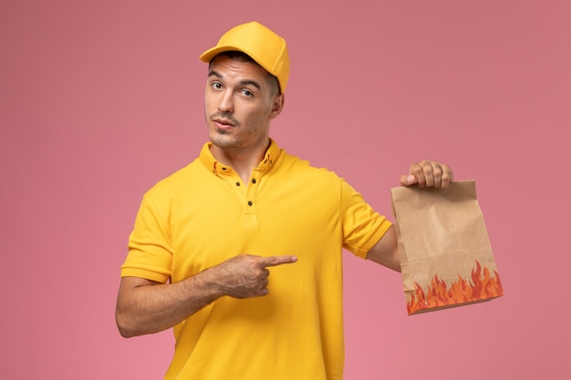 Front view male courier in yellow uniform holding food package on pink background 