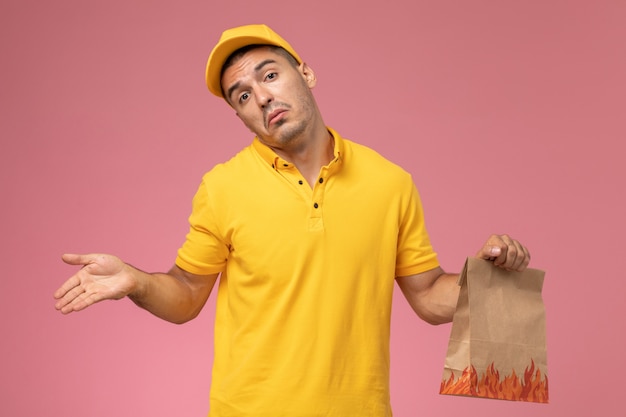 Corriere maschio di vista frontale in pacchetto alimentare giallo uniforme della tenuta con l'espressione confusa sui precedenti rosa