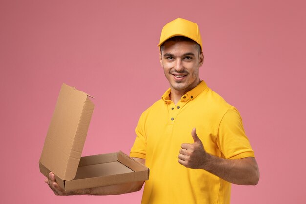 黄色の制服を保持し、明るいピンクの背景に笑みを浮かべて食品宅配ボックスを開く正面男性宅配便