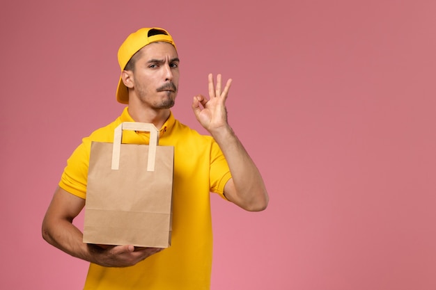 ピンクの背景に紙配達食品パッケージを保持している黄色の制服の正面図男性宅配便。