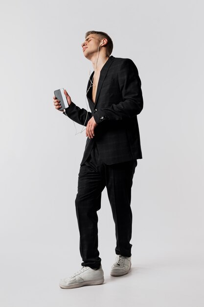 Front view of male dancer in suit and sneakers holding smartphone and headphones