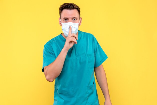 Front view of male doctor asking to be quiet on yellow wall