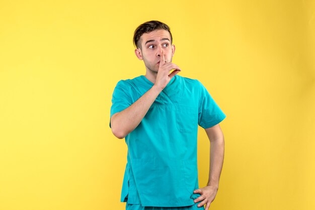 Front view of male doctor asking to be quiet on yellow wall