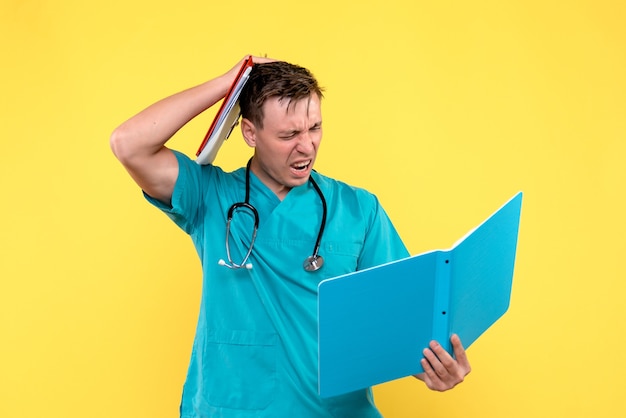 Front view of male doctor checking analyzes on yellow wall