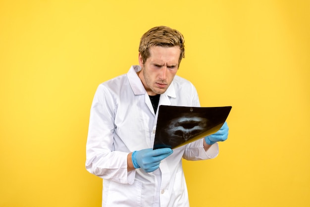 Free photo front view male doctor checking skull x-ray on yellow desk medic surgery covid-