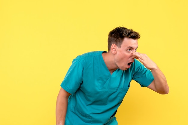 Front view of male doctor closing his nose on yellow wall