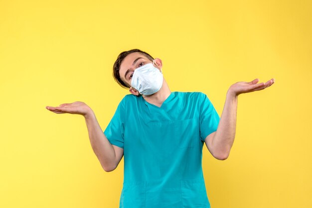 Front view of male doctor confused in sterile mask on yellow wall