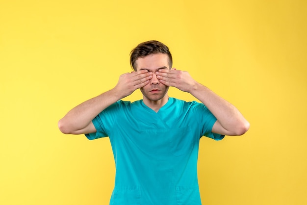 Free photo front view of male doctor covering his eyes on yellow wall