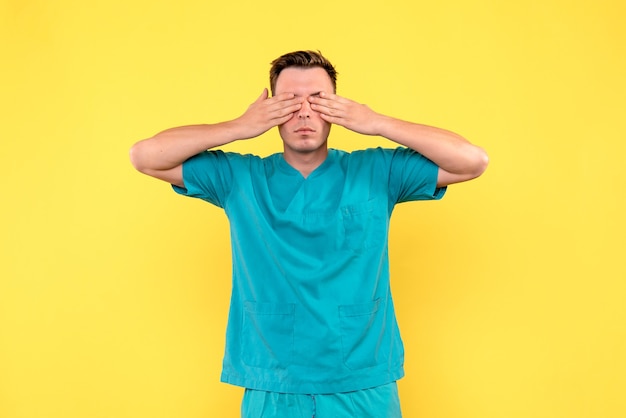 Front view of male doctor covering his eyes on yellow wall