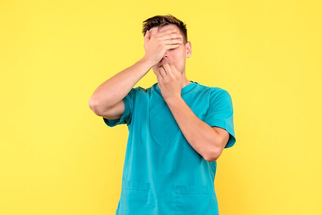 Front view of male doctor covering his face on yellow wall