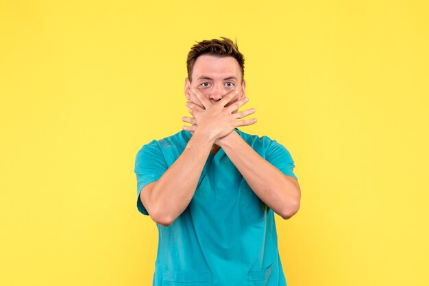黄色い壁に口を覆っている男性医師の正面図