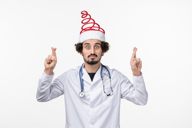 Front view of male doctor crossing his fingers on white wall