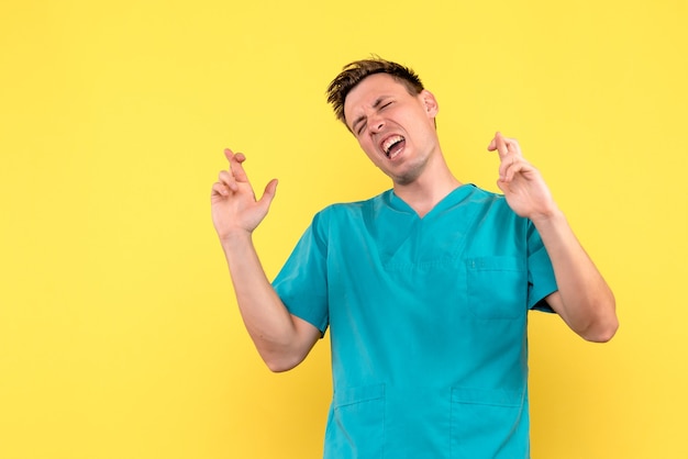 Front view of male doctor crossing his fingers on yellow wall
