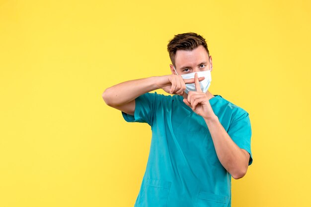 Front view of male doctor crossing his fingers on yellow wall