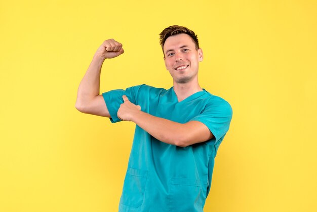 Вид спереди мужского врача, сгибающегося и улыбающегося на желтой стене