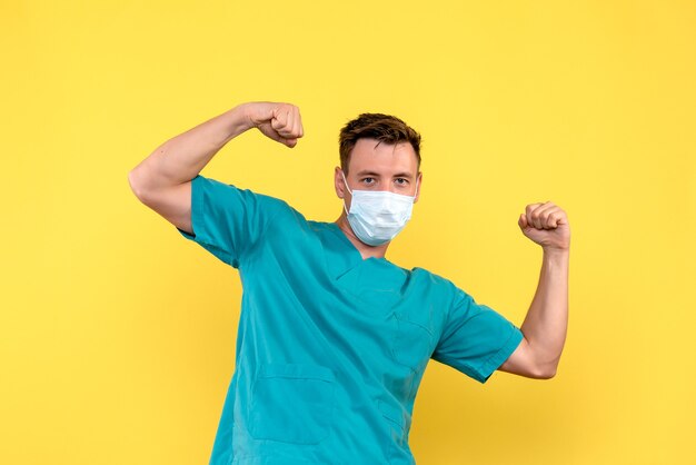 黄色の壁に滅菌マスクで屈曲する男性医師の正面図
