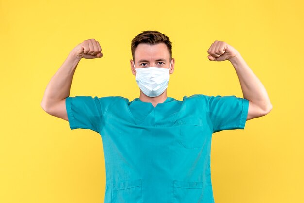 Front view of male doctor flexing with mask on yellow wall