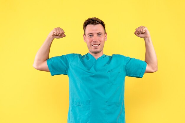 Front view of male doctor flexing with smile on yellow wall