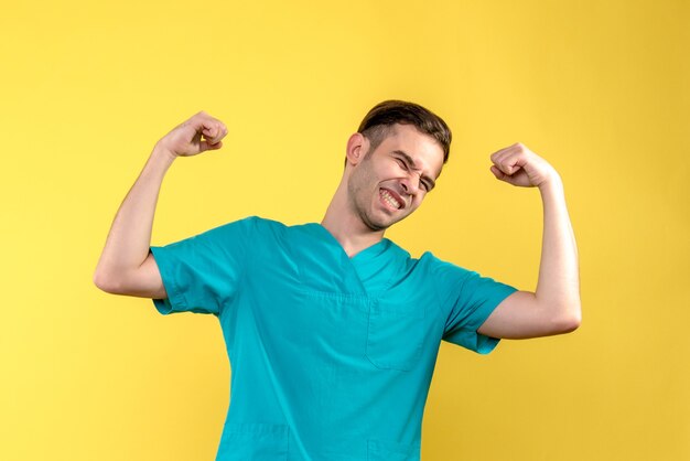 Front view of male doctor flexing on yellow wall