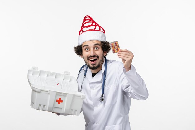 Front view of male doctor getting pills from first aid kit on white wall