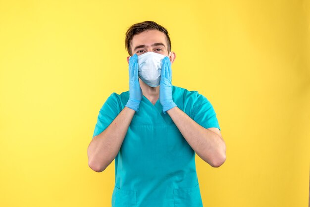 Front view of male doctor in gloves and mask on yellow wall