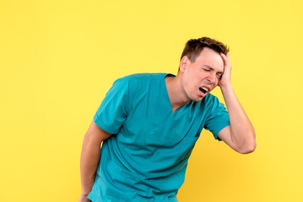 Front view of male doctor having headache on yellow wall