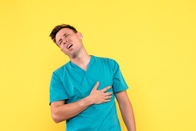 Front view of male doctor having heart problems on yellow wall