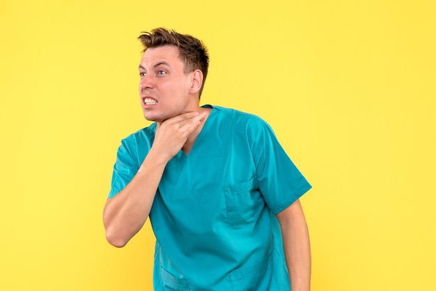 Front view of male doctor having sore throat on yellow wall