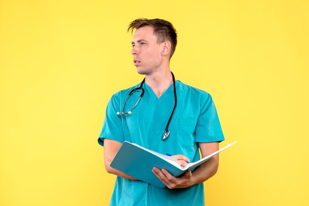 Front view of male doctor holding analyzes in files on a yellow wall