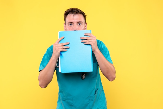Front view of male doctor holding analyzes in files on a yellow wall
