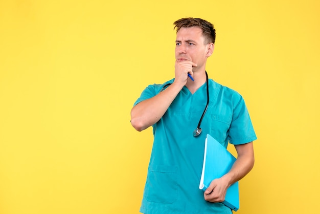 Front view of male doctor holding analyzes in files on yellow wall