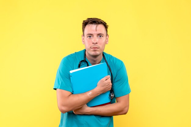 Front view of male doctor holding analyzes on light yellow wall