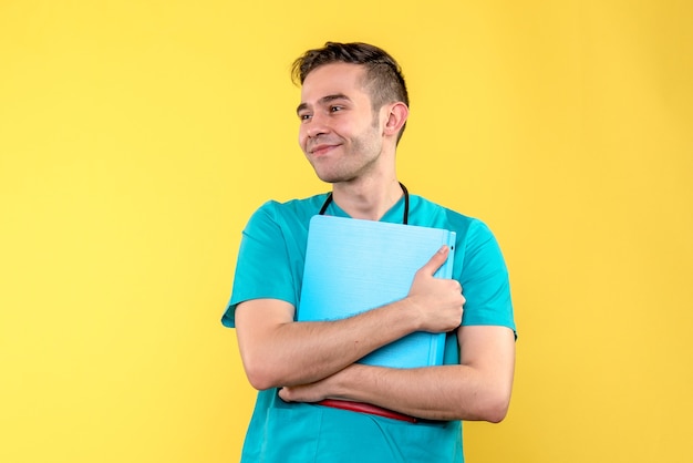 Front view of male doctor holding analyzes on light yellow wall