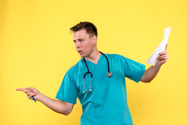 Front view of male doctor holding analyzes on a yellow wall