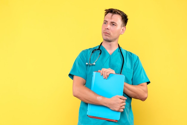 Front view of male doctor holding analyzes on yellow wall