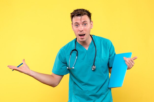 Front view of male doctor holding analyzes on yellow wall