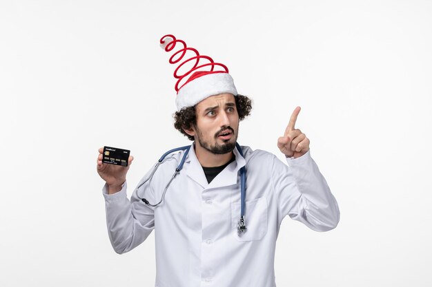 Front view of male doctor holding bank card on the white wall