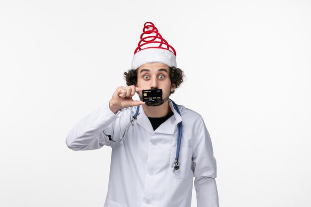 Front view of male doctor holding bank card on white wall