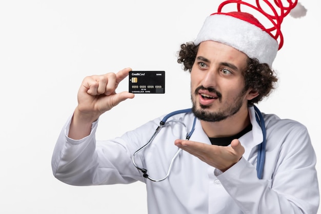 Front view of male doctor holding bank card on white wall