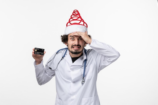 Front view of male doctor holding bank card on white wall