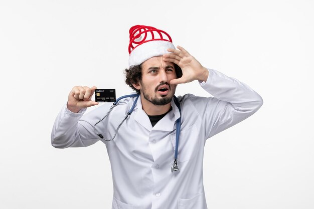 Front view of male doctor holding bank card on white wall