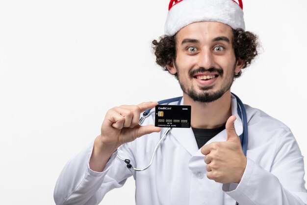 Front view of male doctor holding bank card on white wall