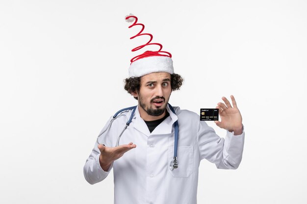 Front view of male doctor holding bank card on white wall