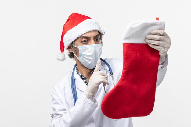 Вид спереди мужчина-врач держит большой праздничный носок на белом столе праздник вируса covid